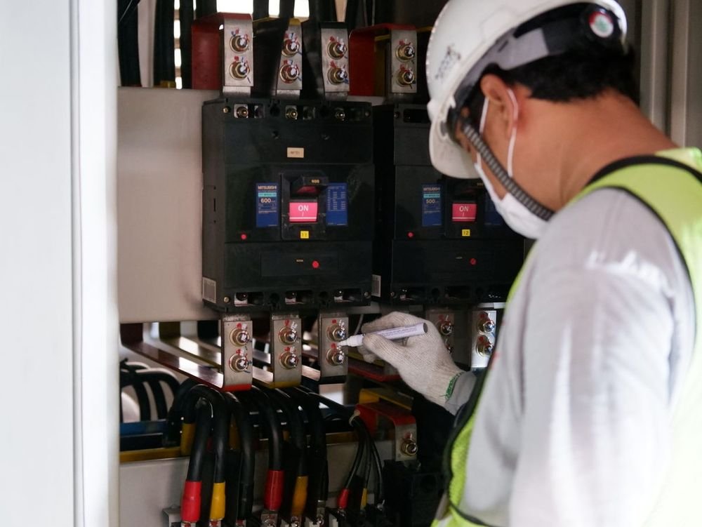 Eletricista com EPI trabalhando em quadro elétrico industrial